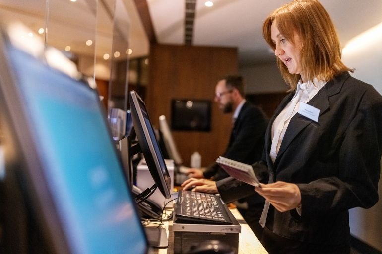 Hotel concierges working at their desk. Receptionist holding passport of and updating guest details in computer system.