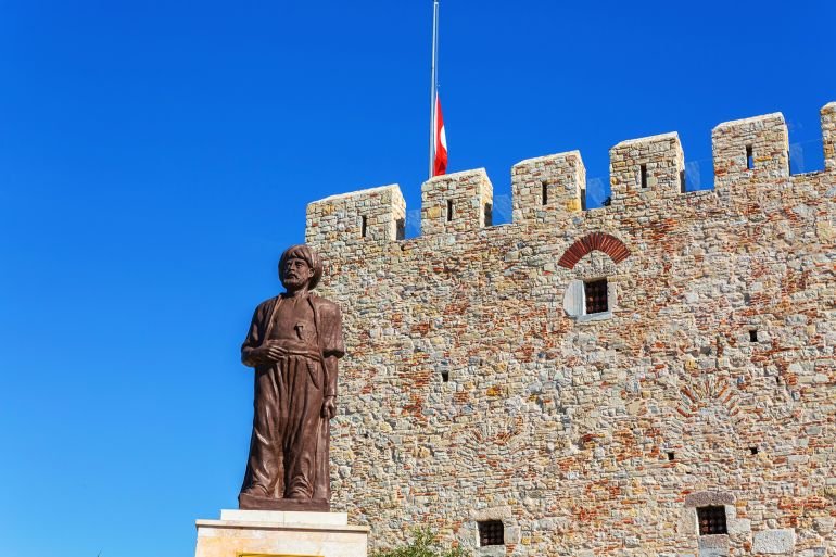 Statue of Hayreddin Barbarossa in front of medieval tower with a Turkish flag, set against a vibrant blue sky in Kusadasi castle. Oct 19, 2023. Kusadasi, Aydin, Turkey (Turkiye)