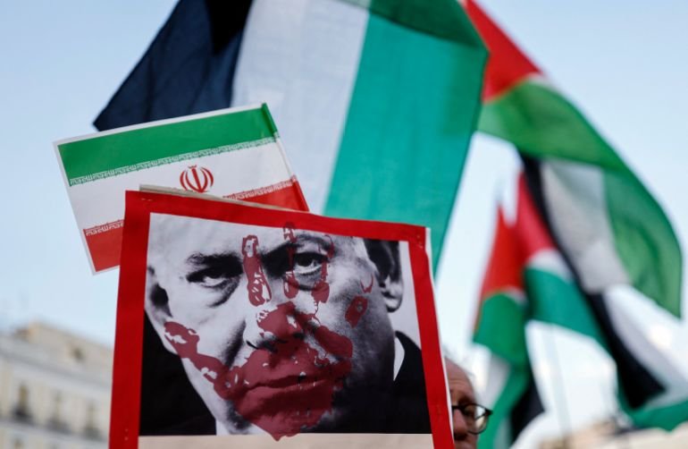 Protestors hold placards showing Israeli Prime minister Benjamin Netanyahu and Iranian and Palestinian national flags during a demonstration in support of Iran and condemnation of Israel's aggression in Madrid, on June 28, 2025.