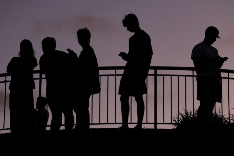 People use their mobile phones, ahead of new law banning social media for users under 16 in Australia, at dusk in Brisbane, Australia, December 8, 2025. REUTERS/Hollie Adams