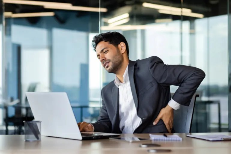 Back pain, businessman working long time sitting at laptop inside office, man massaging back muscle, pain and fatigue, worker in business suit at workplace. المصدر: أدوبي ستوك