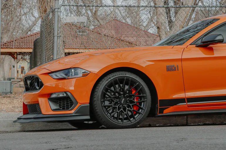 Close-up of an orange Ford Mustang parked outdoors, showcasing luxury and style.