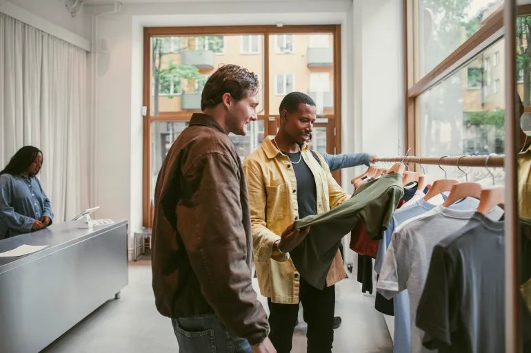 Man looking at t-shirt while shopping with male friend in clothes store - stock photo