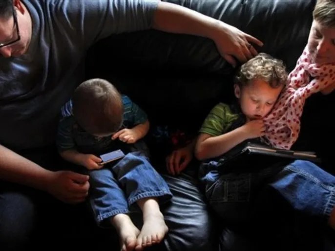 In this Dec. 21, 2011, photo, Joe Hill and his wife Sandy relax with their sons Gunnar, 3, left, and Deacon, 4, as the kids play with an iPhone and an iPad at their home in Norfolk, Va. Joe Hill developed an app called Aeir Talk to help his two sons, who both have autism, express themselves and learn vocabulary.