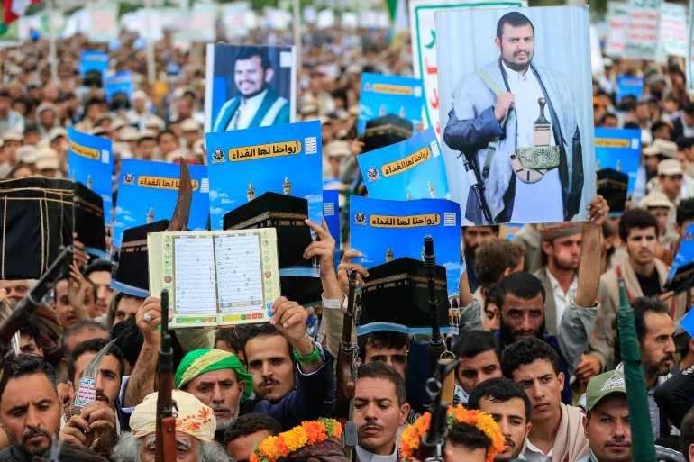 Supporters of the Houthi authorities brandish their weapons and hold up placards showing the Kaaba and reading "For it, we willingly offer our souls" during a protest against the Saudi intervention in Yemen and against Saudi Arabia's recent accusation that the Houthis fired at the holy city of Mecca, in Sanaa on September 18, 2026.