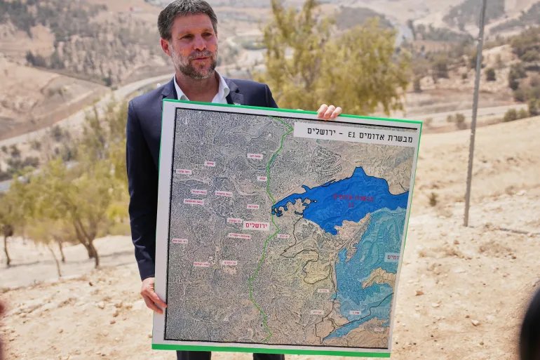 CORRECTS DAY Israeli Finance Minister Bezalel Smotrich holds a map that shows the E1 settlement project during a press conference near the settlement of Maale Adumim, in the Israeli-occupied West Bank, Thursday, Aug. 14, 2025. (AP Photo/Ohad Zwigenberg)