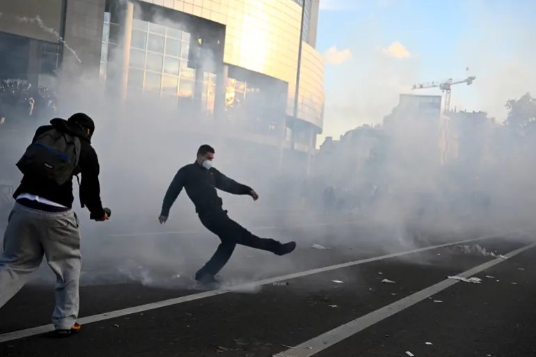 A protester kicks a tear gas canister during a demonstration of high-school students at Place de la Bastille, in Paris, on October 8, 2026, as part of a nationwide protest movement over learning conditions. Since late September, pupils have barred the entrances to hundreds of schools, complaining of teacher absences, overloaded timetables, dilapidated classrooms and buildings ill-adapted to rising temperatures, among other grievances. (Photo by JULIEN DE ROSA / AFP)