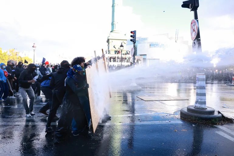 Protesters face a water cannon during a demonstration of high-school students at Place de la Bastille, in Paris, on October 8, 2026, as part of a nationwide protest movement over learning conditions. Since late September, pupils have barred the entrances to hundreds of schools, complaining of teacher absences, overloaded timetables, dilapidated classrooms and buildings ill-adapted to rising temperatures, among other grievances. (Photo by Kenzo TRIBOUILLARD / AFP)