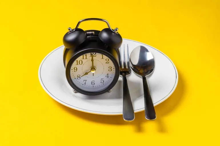 Empty plate with clock on a yellow background, intermittent fasting concept; Shutterstock ID 2729032267; purchase_order: aj; job: ; client: ; other: