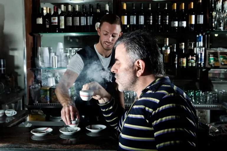 A man enjoys his hot coffee or espresso in a bar. It looks classical and tasty. He really enjoys the drink and his break.