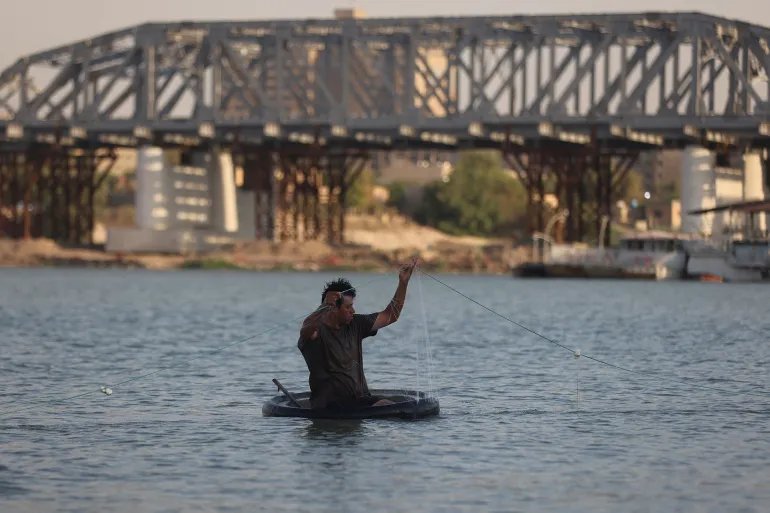 TOPSHOT - An Iraqi fisherman in an inflatable craft hauls in his net on the Tigris River in central Baghdad on August 18, 2026. (Photo by AHMAD AL-RUBAYE / AFP)