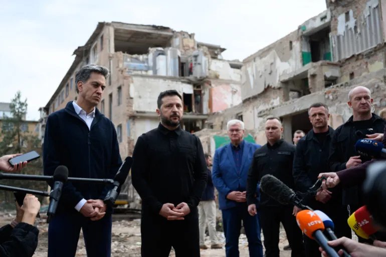 This handout photograph taken and released by Ukrainian Presidential Press Service on October 8, 2026, shows Ukraine's President Volodymyr Zelensky (2nd L) and Britain's Foreign Secretary Ed Miliband (L) speaking to media during during their visit to a flattened five-storey apartment a day after a Russian missile attack in Pryluky, Ukraine.